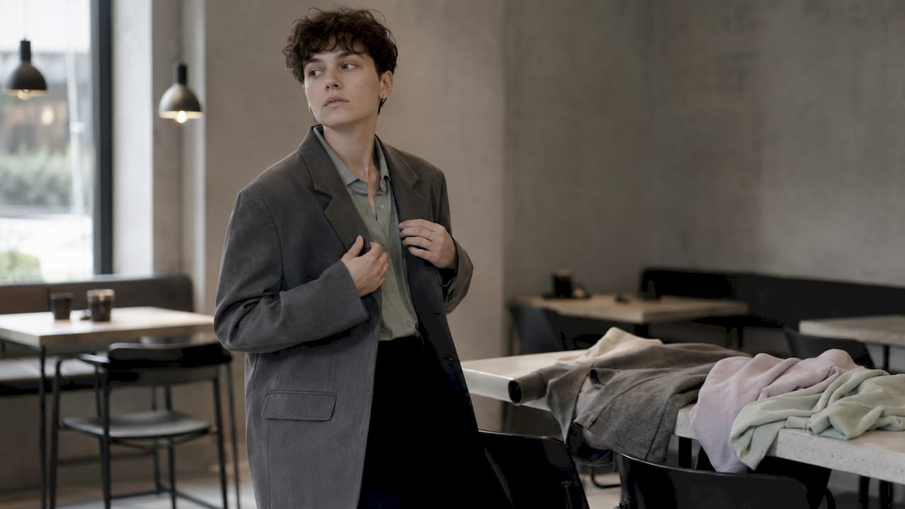Eine Person in einem genderfluiden Outfit richtet ihren Blazer zurecht.
