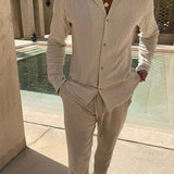 Mann trägt beiges Sommer-Set aus Leinen mit lockerem Hemd und Hose, vor modernem Pool – ideal für warme Tage und stilvolle Freizeitlooks